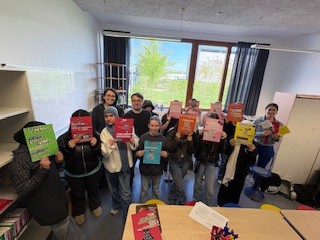 Schülerinnen und Schüler zeigen mit der Workshopleitung und der Lehrkraft ihre Ergebnisse des Workshops. 